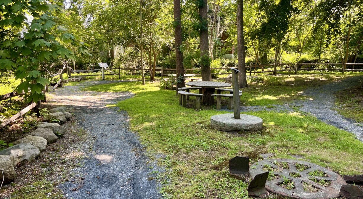 A photograph of a small park with historic mill equipment and a gravel trail.
