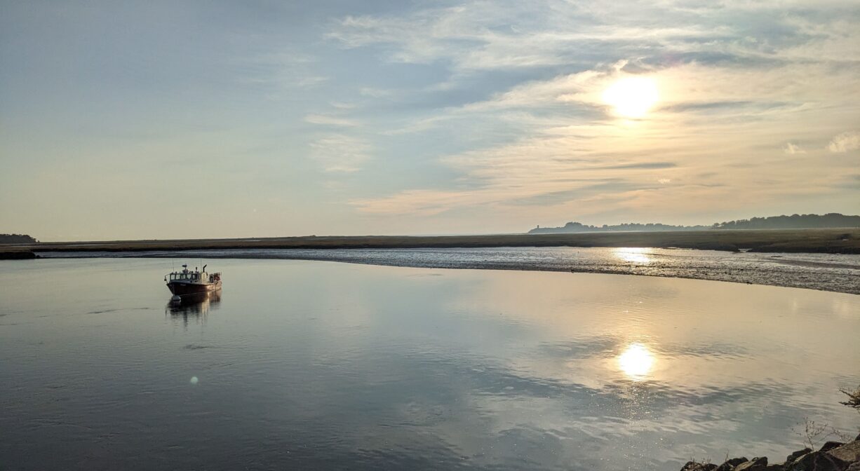A photograph of a single boat on a still river at sunrise.