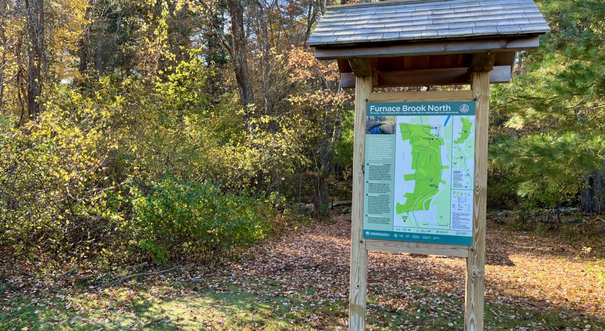 A photograph of an informational kiosk at a trailhead with colorful foliage.