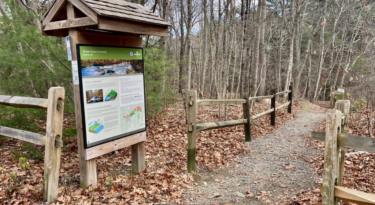 A photograph of a forest trailhead with a wooden kiosk.