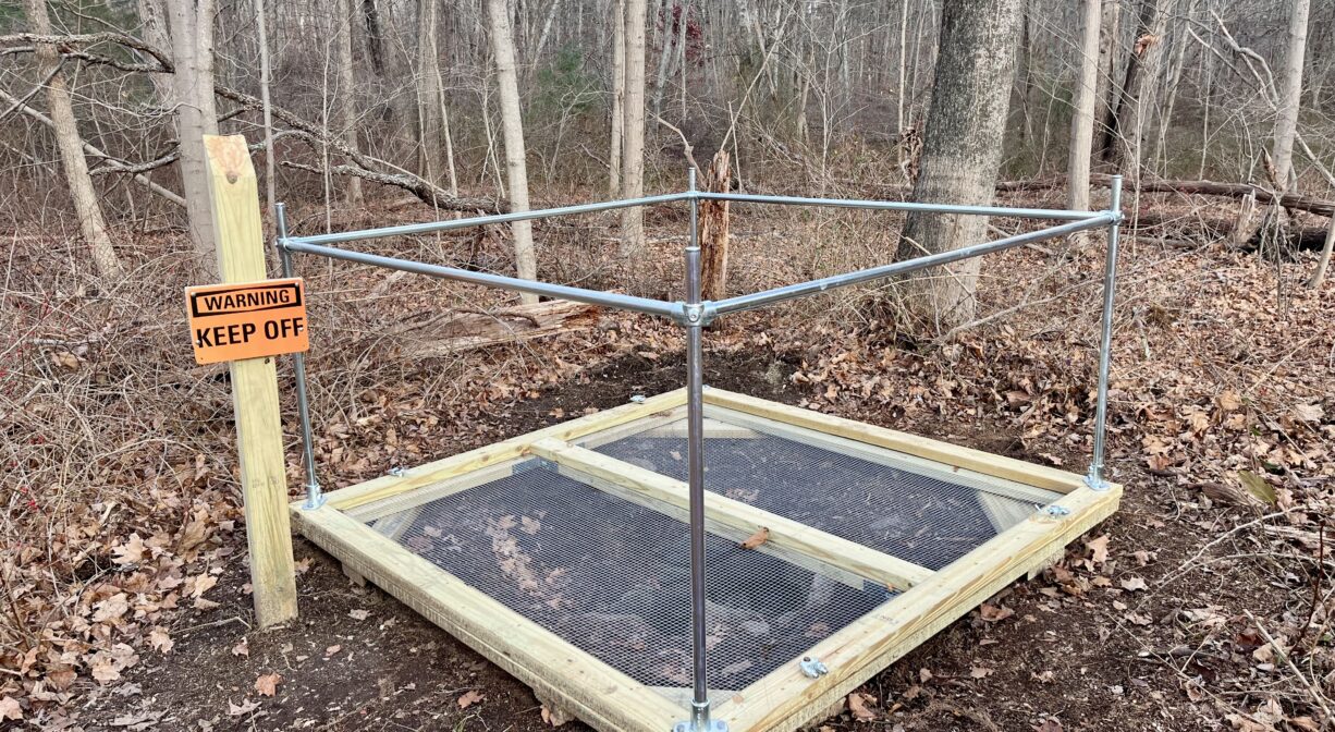 A photograph of a wood and metal structure on a forest floor.
