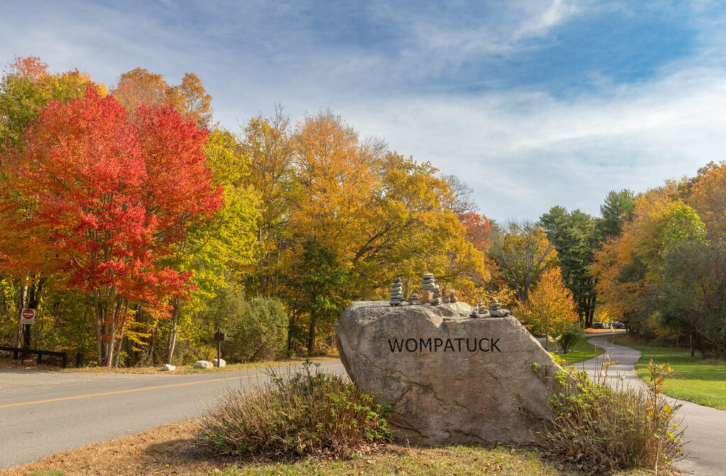 A park entrance with a boulder property sign and colorful foliage.