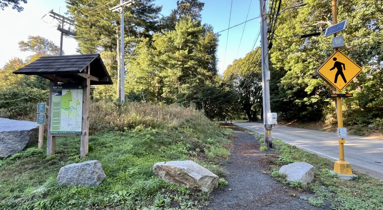 A photograph of an informational kiosk and a road crossing, with a trailhead.