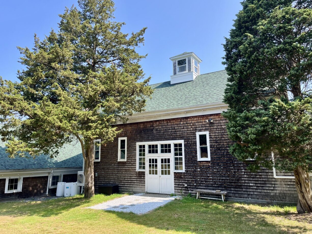 A photograph of a barn with cedar trees to either side.