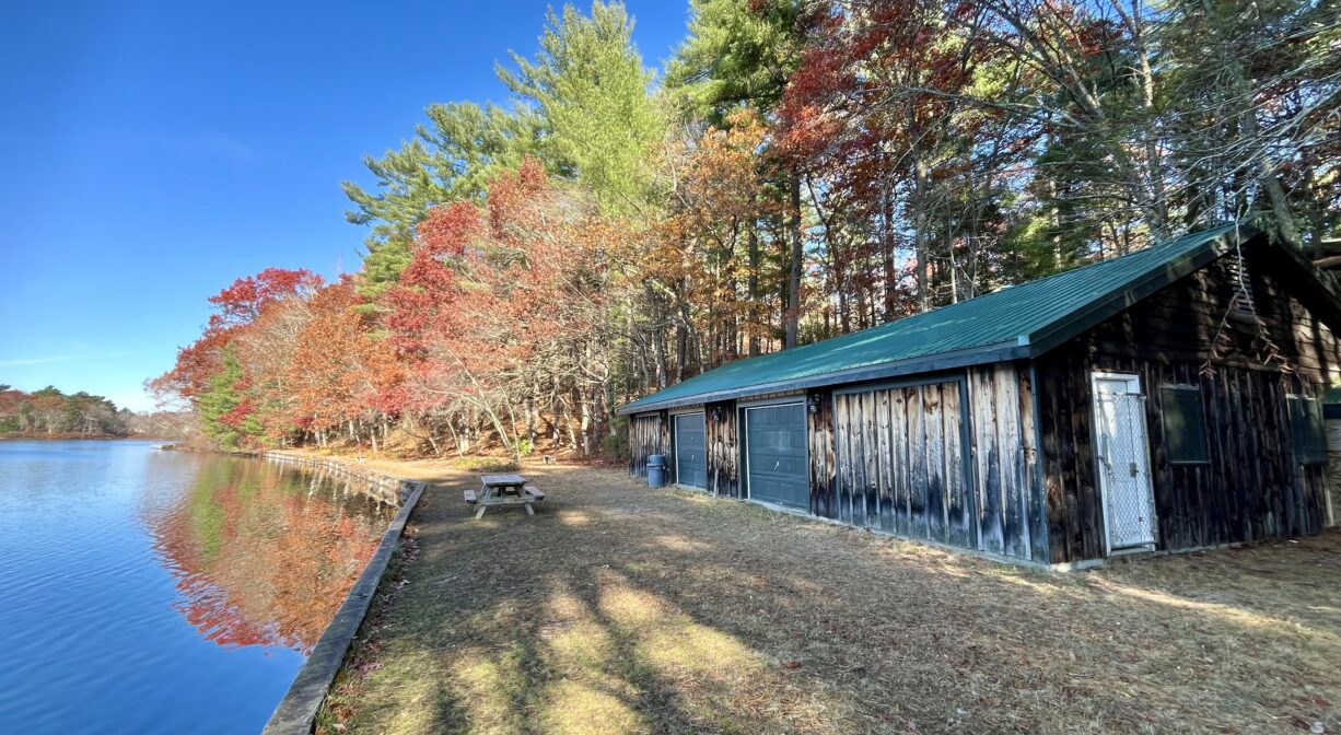 A photograph of a storage building beside a pond, with colorful trees.