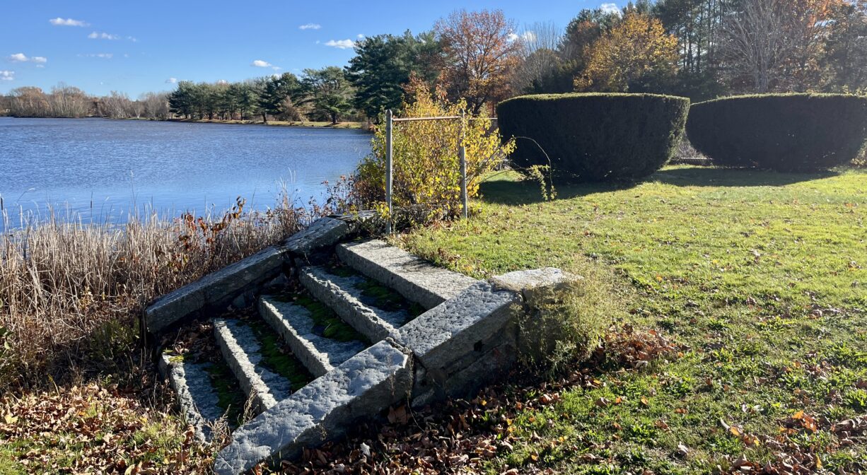 A photograph of a short granite staircase leading up a grassy hill next to a pond.