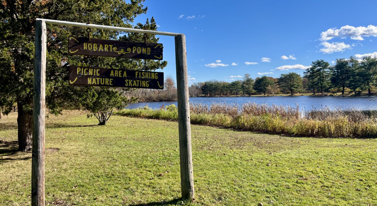 A photograph of a property sign in a grassy park by a pond.