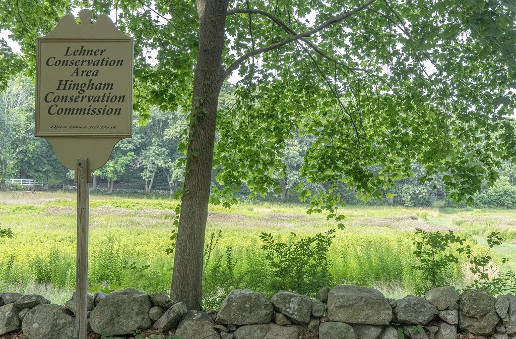 A photograph of a property sign and a stone wall, with a meadow in the background.