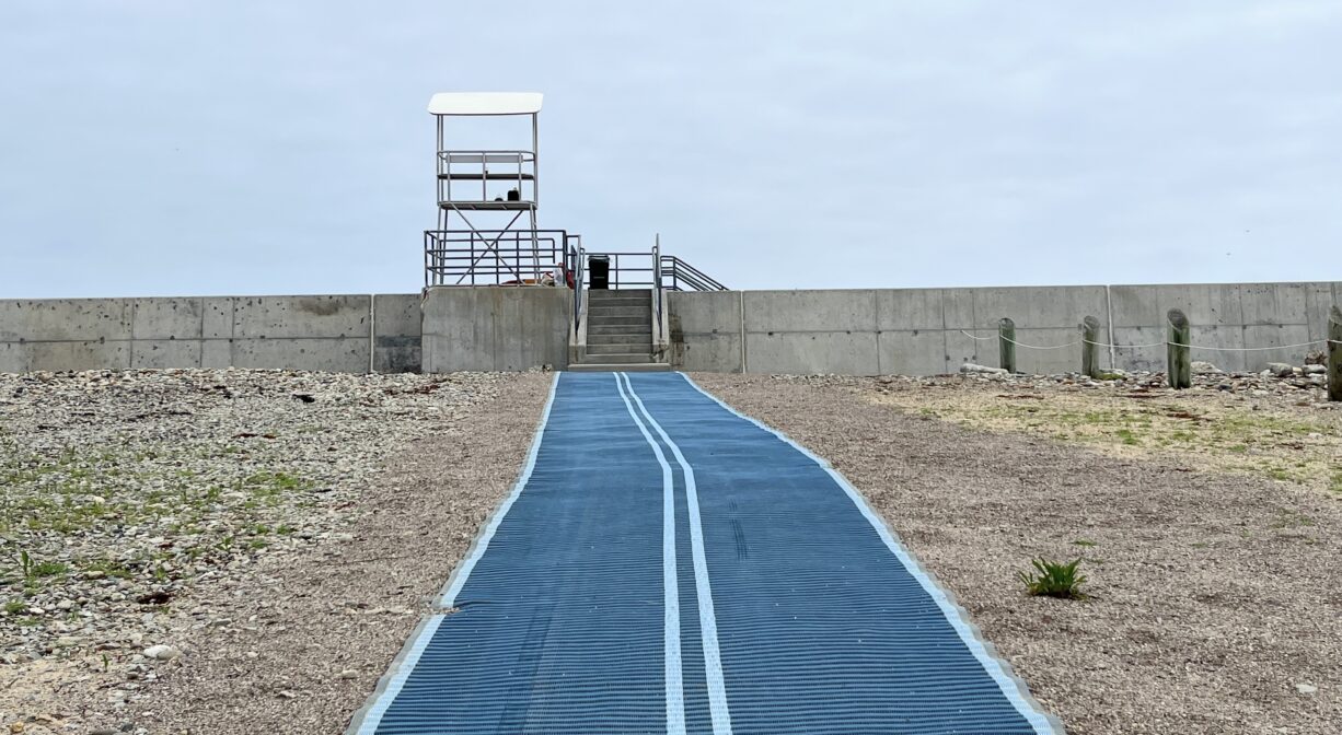A photograph of an accessibility mat that leads to a seawall.