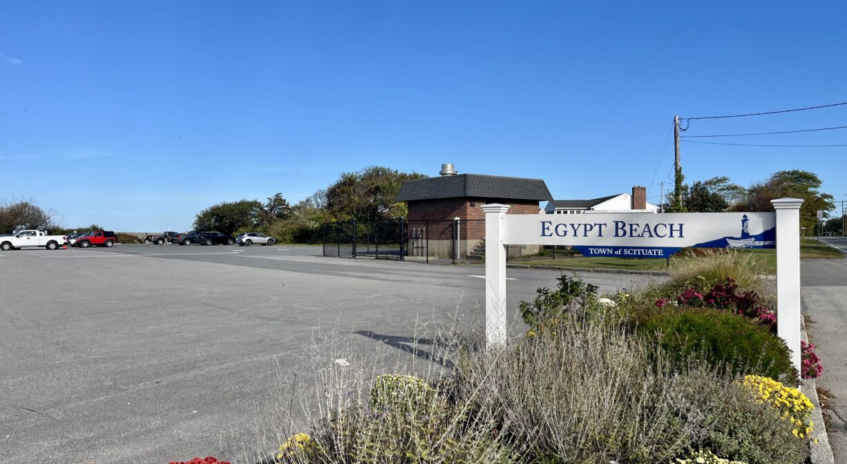 A photograph of a property sign beside a large paved parking area.