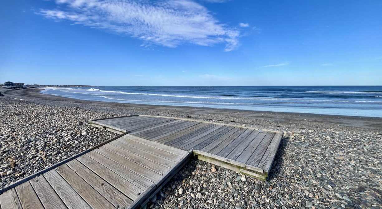 A photograph of a wooden platform on a stony ocean beach.