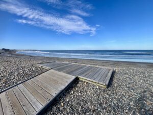 A photograph of a wooden platform on a stony ocean beach.