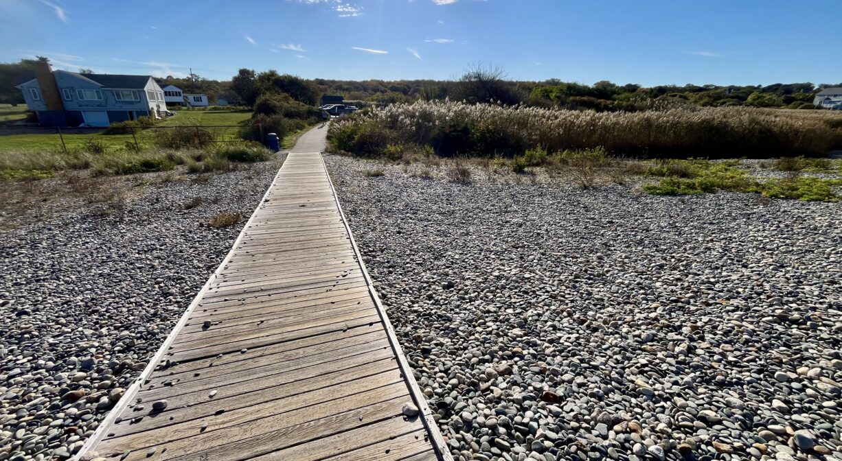A photograph of a boardwalk leading down a stony hill to a parking area.