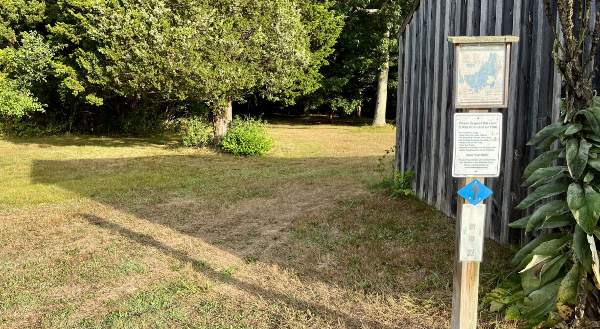 A photograph of a trailhead next to a barn, with interpretive signage.