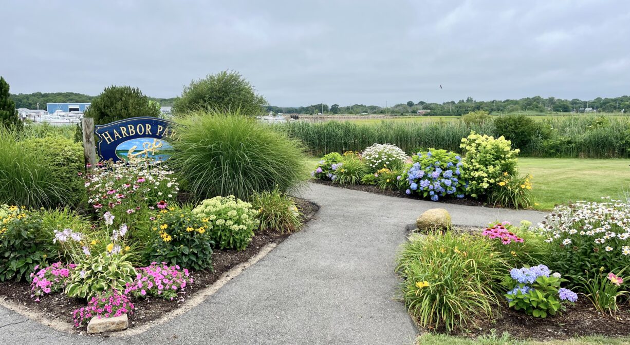 A photograph of a park entrance with a property sign and numerous flowering plants.