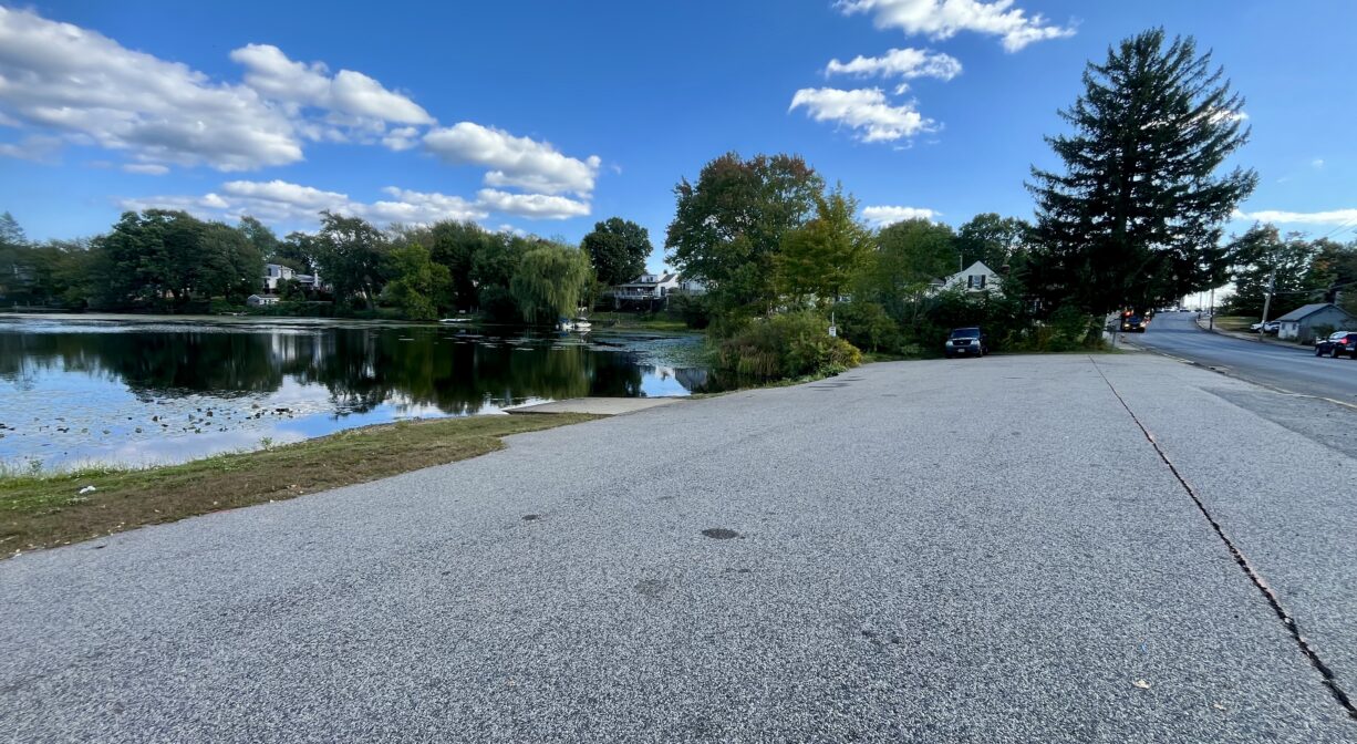 A photograph of a paved parking area beside a pond.