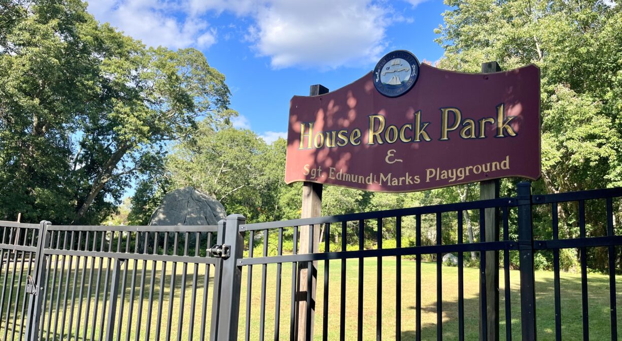 A photograph of a park with a sign and a metal fence.