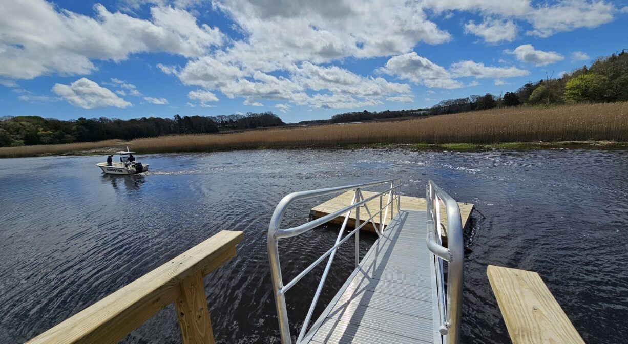 A photograph of a ramp and a float on a river with a boat in the distance.
