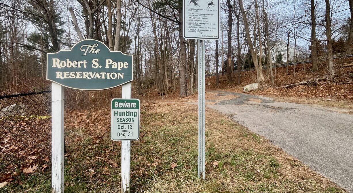 A photograph of a trailhead and property sign with grass in the foreground and trees in the background.
