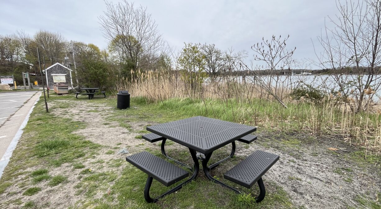 A photograph of a series of picnic tables with water in the background.