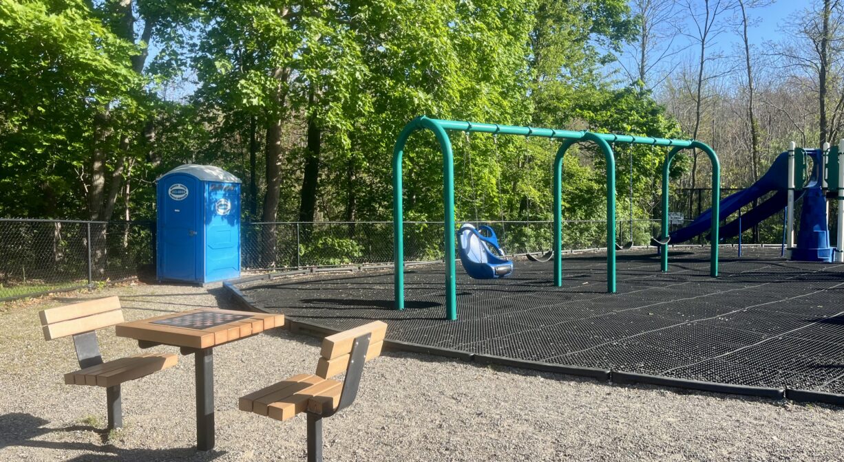 A photograph of a playground with a portable toilet and a picnic table.