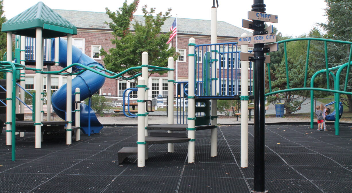 A photograph of a playground with a large brick building in the background.