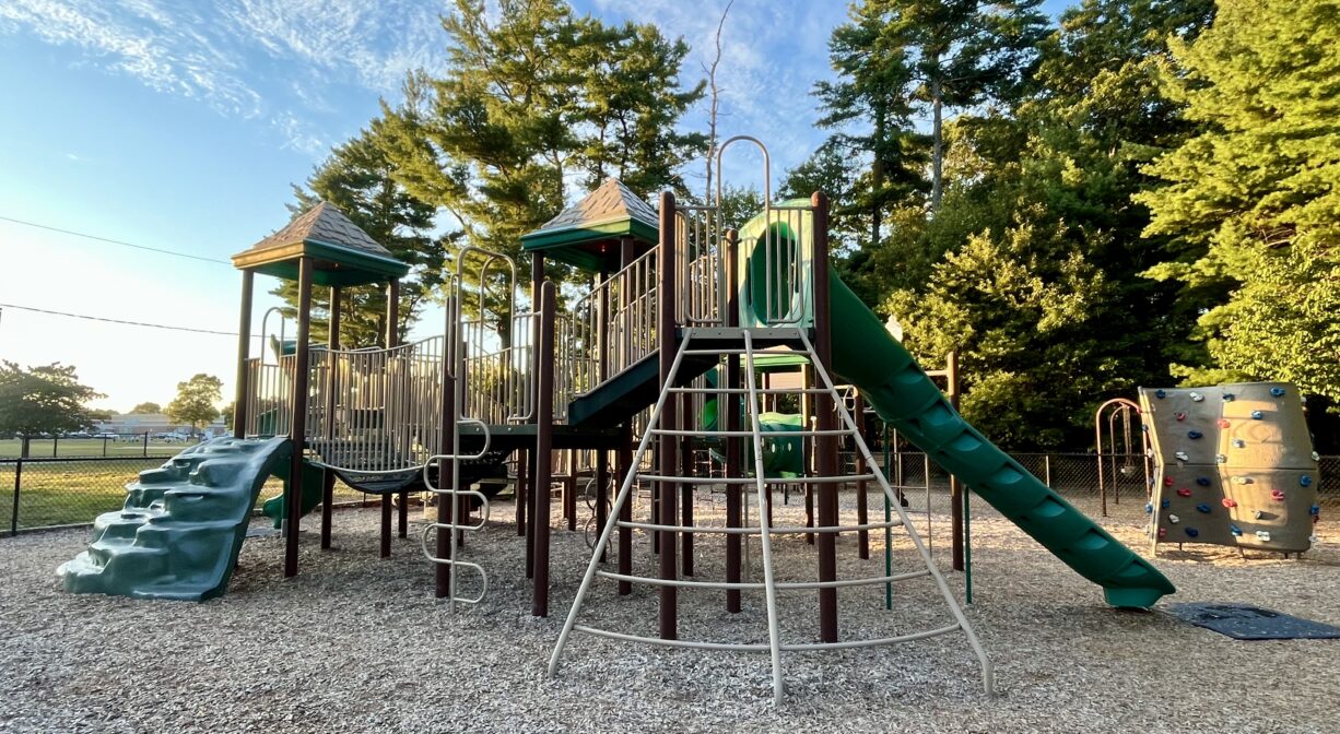 A photograph of a playground with green and brown play structures.