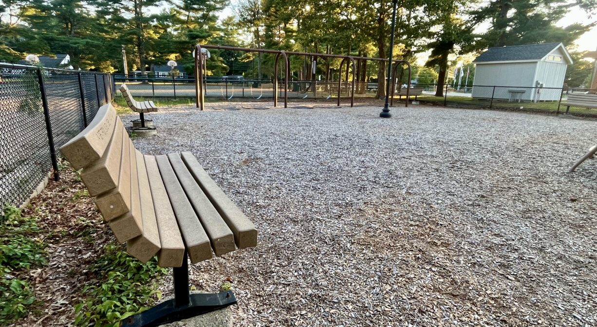 A photograph of a playground with a bench in the foreground and a row of swings in the background.