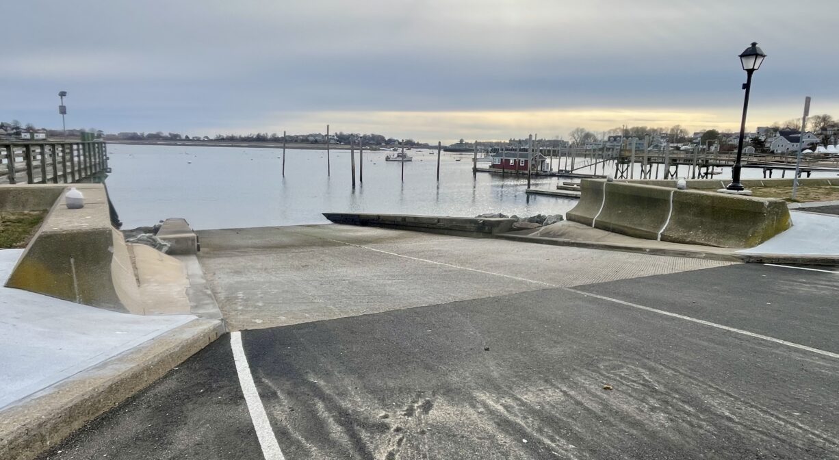 A photograph of a concrete and asphalt boat ramp on a harbor.
