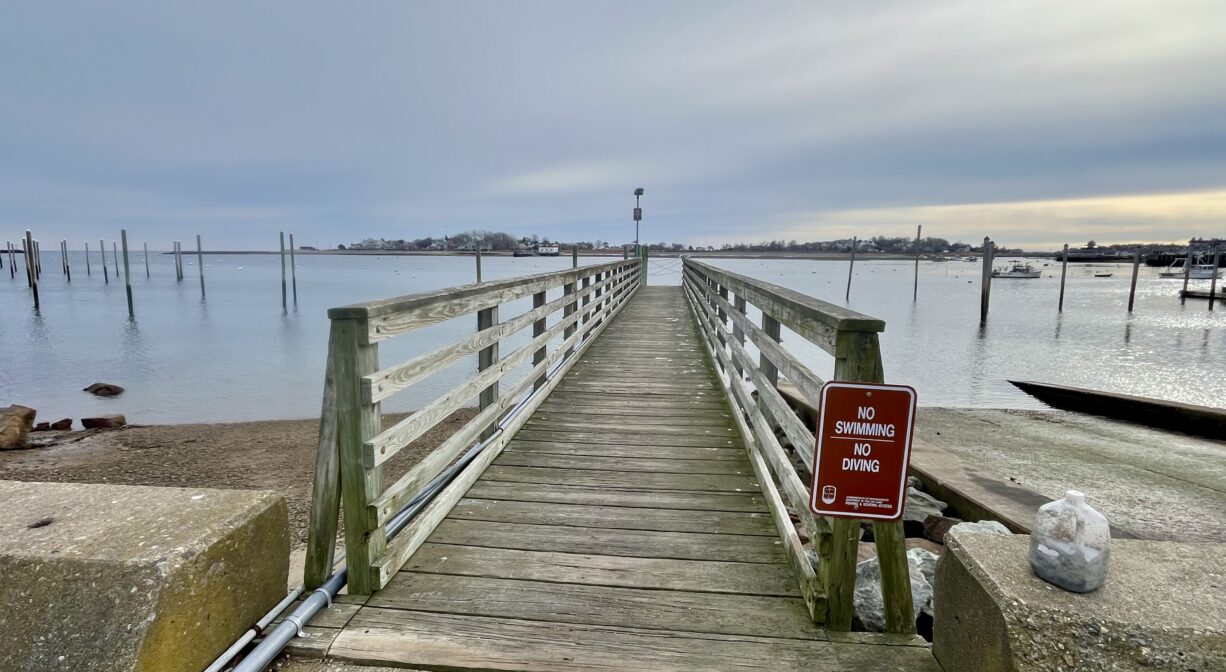 A photograph of a wooden walkway and pier extending into a harbor.