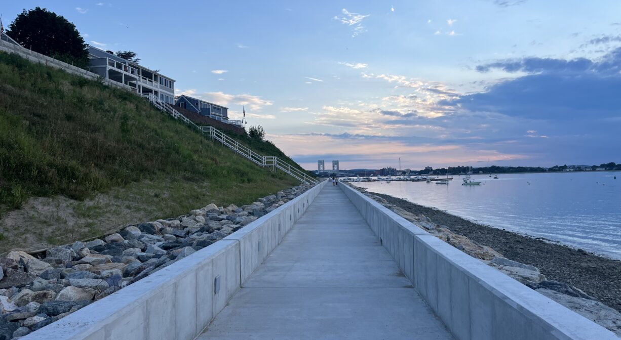 A photograph of a long concrete walkway on a shoreline at sunset.