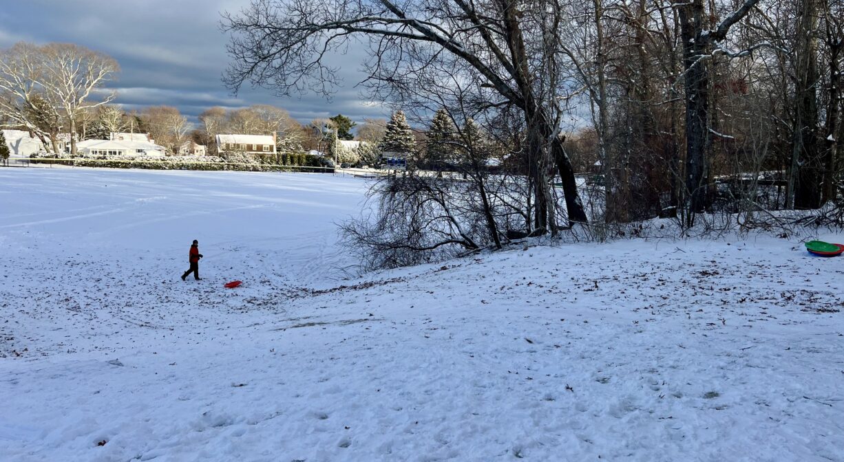 A photograph of a sow covered hill with a person and a sled at the bottom.