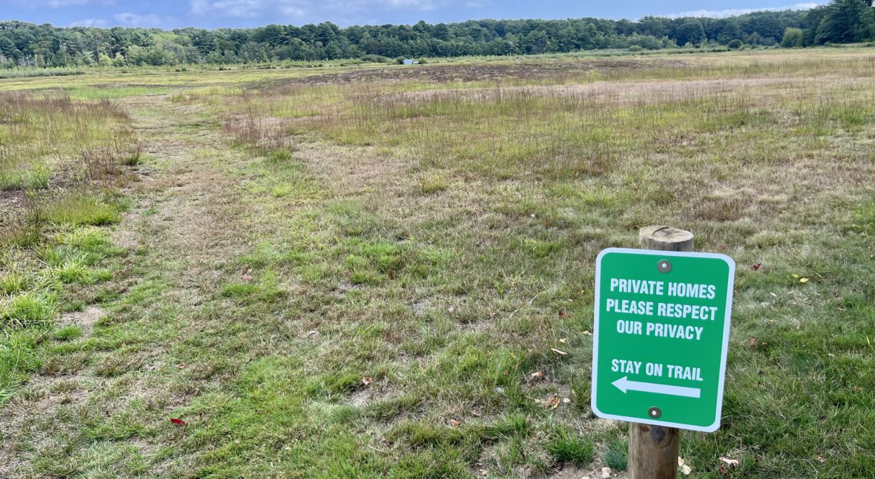 A photograph of a trail usage sign alongside a grassy trail.