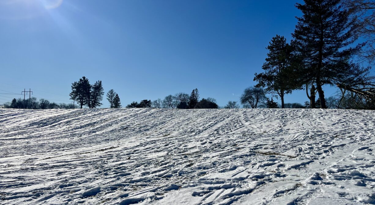 A photograph of a snow-covered hill with numerous footprints.