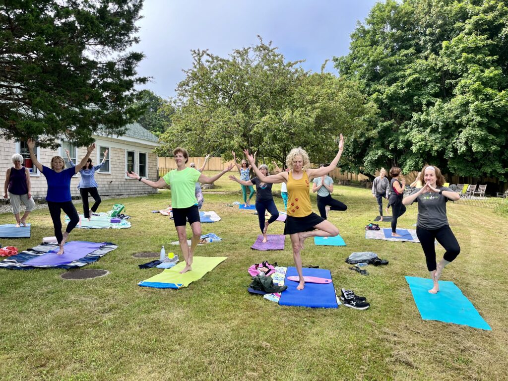 A photograph of a yoga class on a lawn with trees in the background.