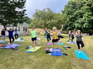 A photograph of a yoga class on a lawn with trees in the background.