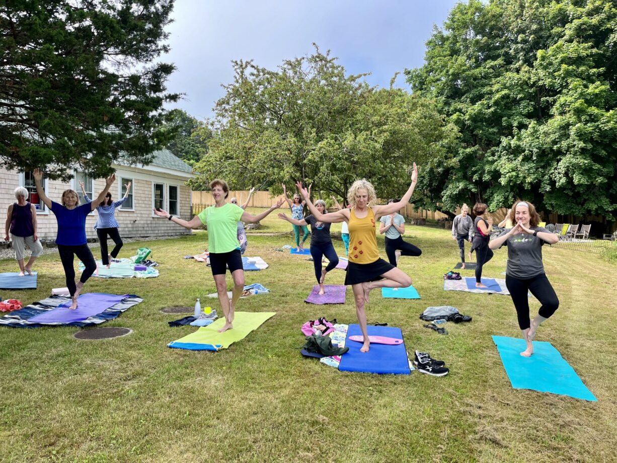 A photograph of a yoga class on a lawn with trees in the background.
