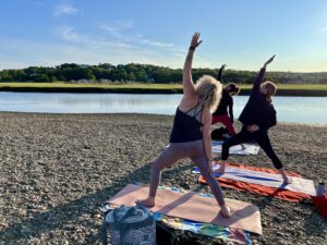 A photograph of three people doing yoga beside a river.