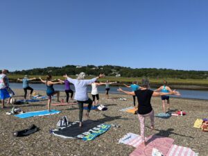 A photograph of a group of people doing yoga beside a river.