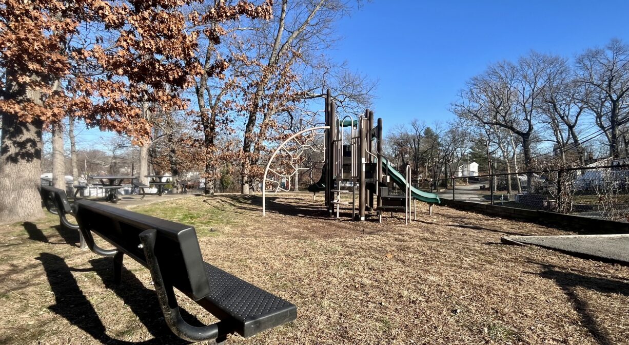 A photograph of a small playground with a bench and play equipment.