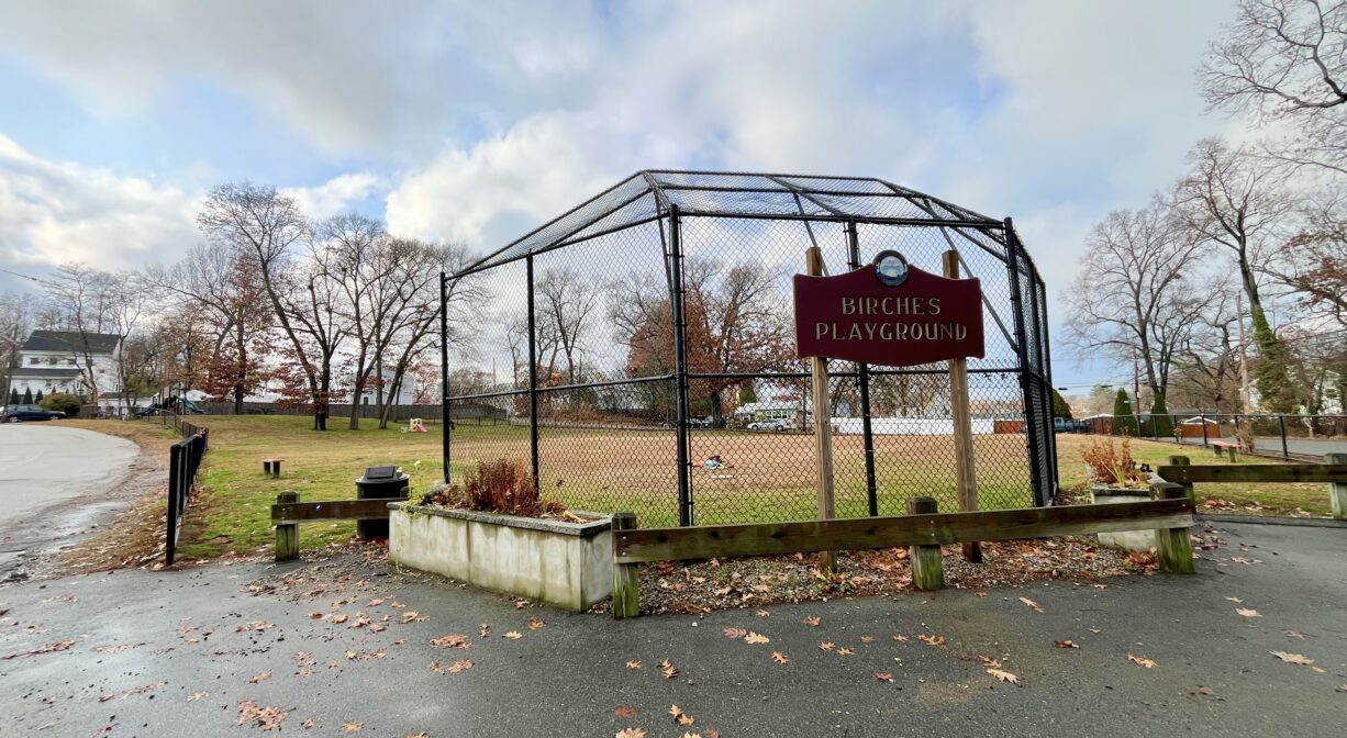 A photograph of a backstop with a property sign on it and parking spots in the foreground.