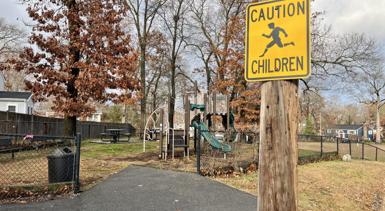 A photograph of a paved walkway leading into a park, with a Caution Children sign in the foreground.