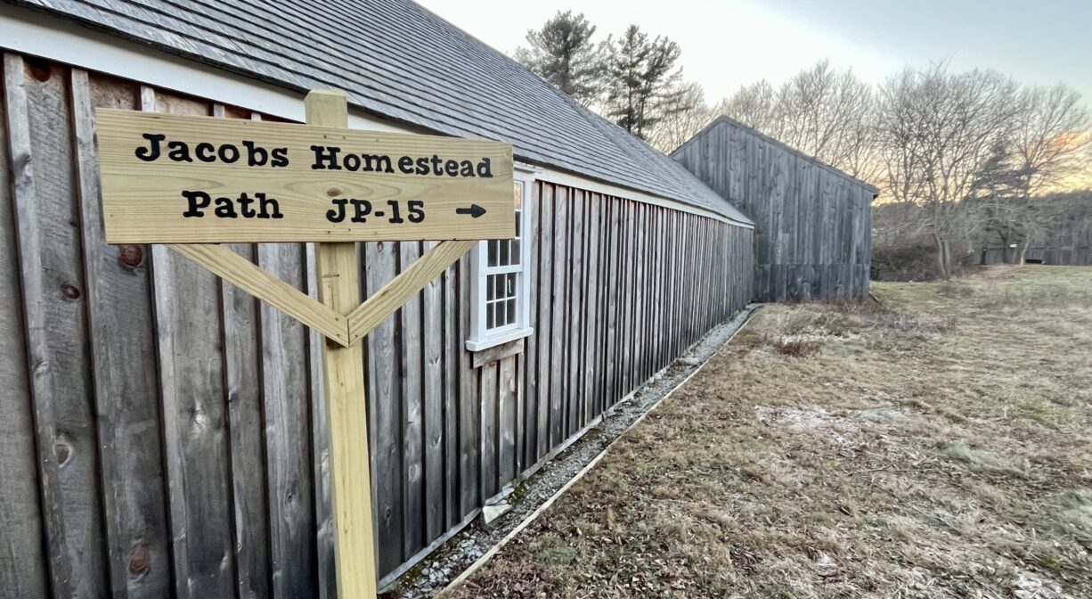 A photograph of a trail sign and a historic building beside an open field.