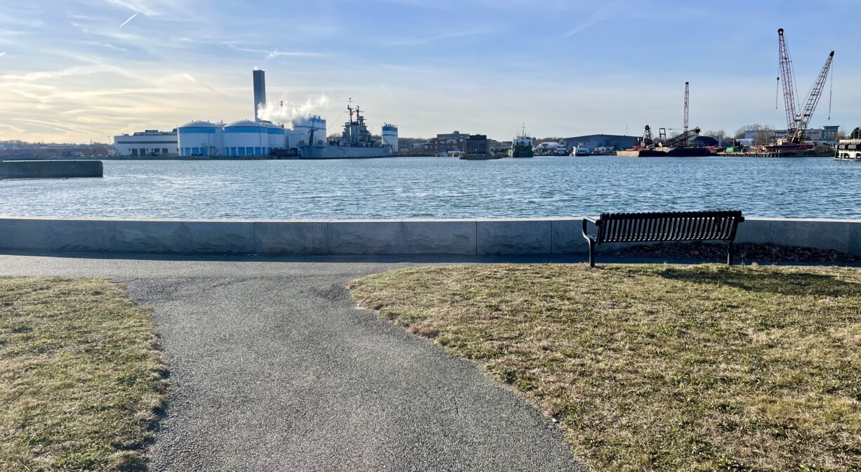 A photograph of a paved trail leading through a park to a river.