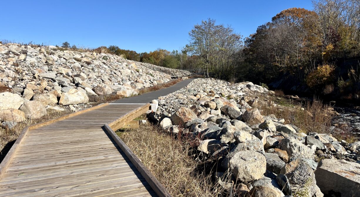 A photograph of a boardwalk and a paved trail extending through a rocky area.