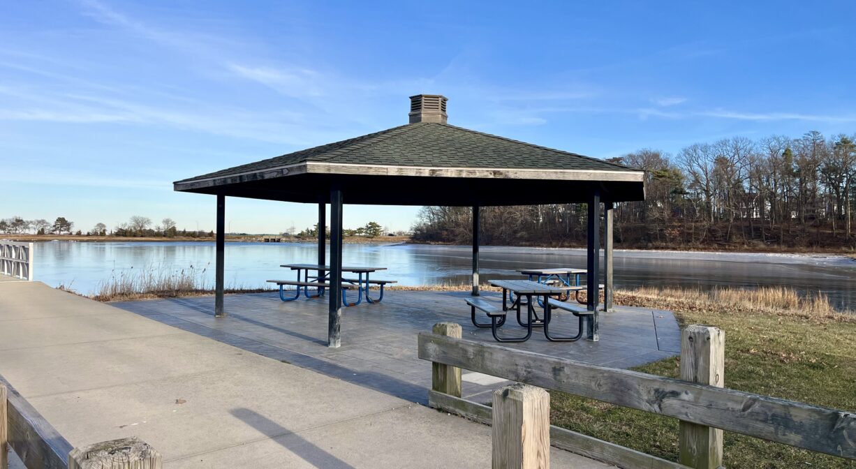 A photograph of a shaded picnic pavilion beside a marsh creek.