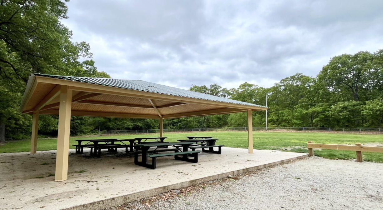 A photograph of a picnic pavilion beside a soccer field and a playground.