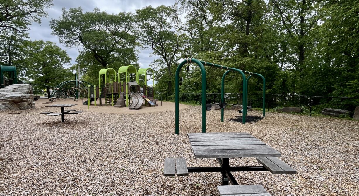 A photograph of a playground with green play equipment and a picnic table.