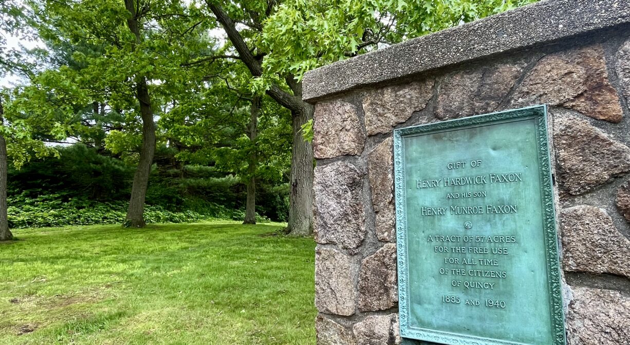 A photograph of a park with a stone wall and a metal property sign.