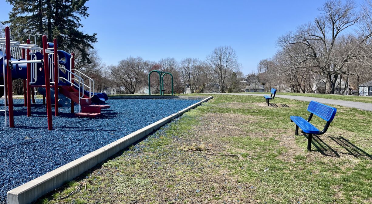 A photograph of a park with a playground and a bench.
